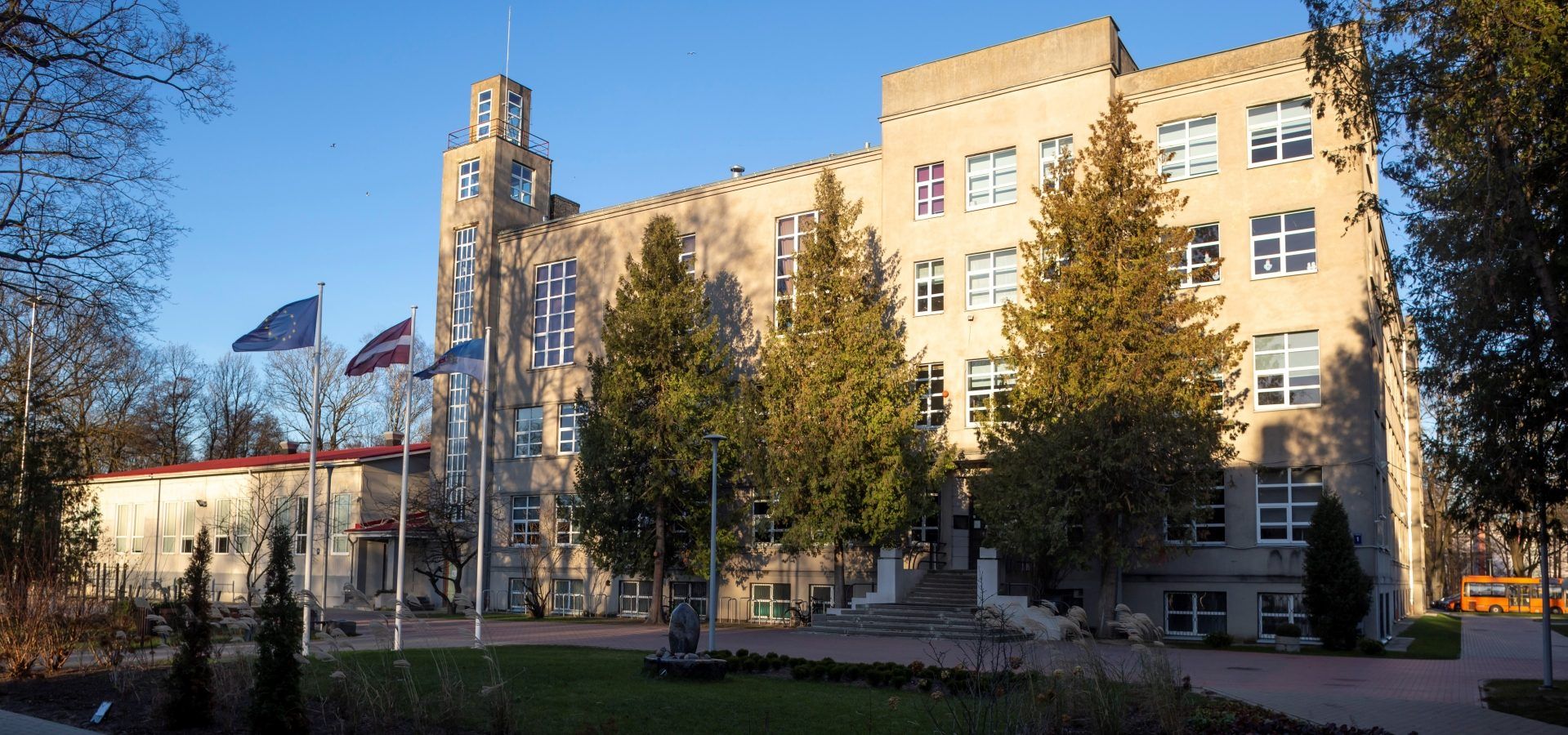 Skolas ēka ar torni, karogiem un kokiem