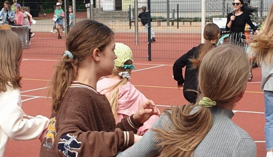 Skolēni sarkanā sporta laukumā skatās pasākumu