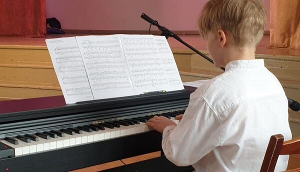 A boy in a white shirt plays the piano in front of the stage and reads music