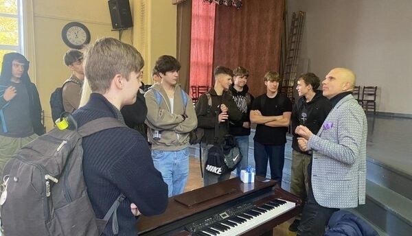 Pupils listen to a man at an electric piano in a hall